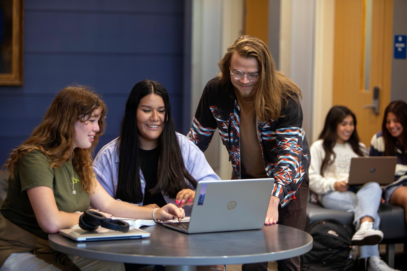 Three students gathered around a laptop, engaged in discussion